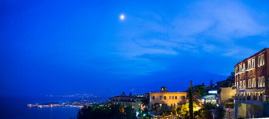 Mount Etna Volcano and the moon at night, panoramic view seen from Piazza IX Aprile on Corso Umberto, the main street in Taormina, Sicily, Italy, Europe