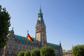 Hamburger Rathaus mit Deutscher Flagge bei Sonnenschein und blauem Himmel