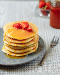Homemade pancakes with honey and strawberries on a gray plate with a fork beside