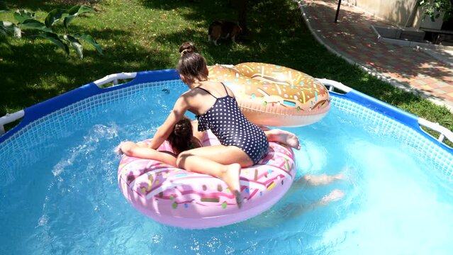 Kids have fun floating on swim ring in outdoor swimming pool on sunny summer day, leisure