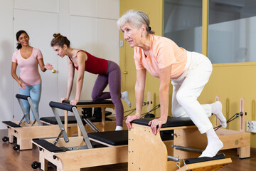 Portrait of focused elderly woman practicing pilates in fitness studio, doing stretching exercises on wunda chair