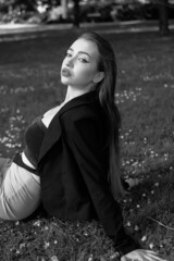 Black and white portrait of a young girl in the city park. Elegant and melancholy portrait, the girl is sitting on the grass. Beautiful woman in classic clothes