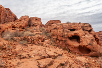 Fototapeta na wymiar Overton, Nevada, USA - February 25, 2010: Valley of Fire. Landscape featuring potholed, lined red rock with caves among other boulders under heavy rainy gray cloudscape. 