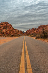 Fototapeta na wymiar Overton, Nevada, USA - February 25, 2010: Valley of Fire. Straight double yellow line divide asphalt road between red rock mountains under heavy rainy gray cloudscape.