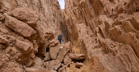 Hiking path inside a narrow slot in a remote region of Negev desert. Male hiker descending from a...