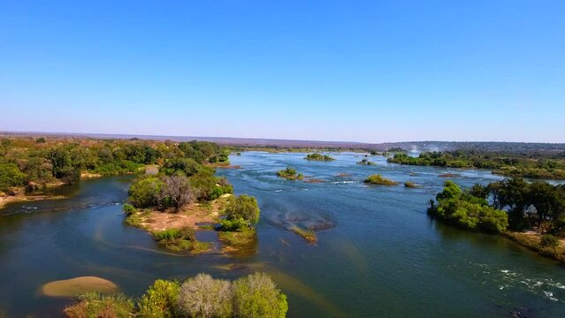 Aerial view of the Zambezi River flowing around Victoria Falls, showcasing dramatic waters, lush surrounding landscapes, and the iconic waterfall. Ideal for nature, travel, and adventure projects.