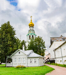 Fototapeta na wymiar Wide panoramic view of an old wooden house and trees inside the kremlin of Vologda, in front of the bell tower and cloudy sky