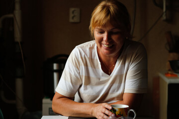 Defocus happy young caucasian woman smiling while sitting at home with coffee or tea mug. Morning routine in kitchen. Home lifestyle. Happy 40 years woman at home. Out of focus