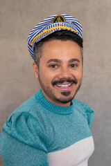 LGBT man boy wearing a marine hat and a blue sweather, smiling and posing for the camera by a grey background in a studio. 