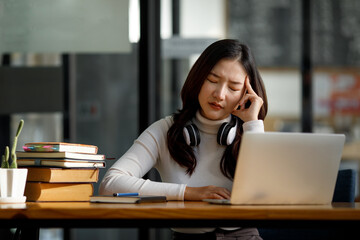 Asian women sitting in a home office With stress and eye strain.Tired businesswoman holding eyeglasses and massaging nose bridge. There are tablets, laptops, and coffee.