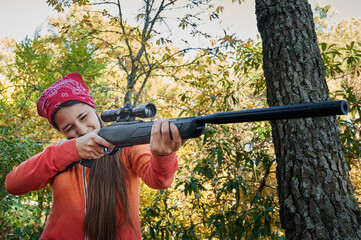 Sideview of teenage woman dressed in colorful clothing wields a shotgun while aiming using a...