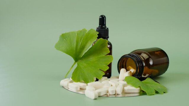 ginkgo biloba leaf ,white tablets and liquid ginkgo biloba extract in brown glass jars on green background.Preparations with ginkgo biloba extract. 4k footage