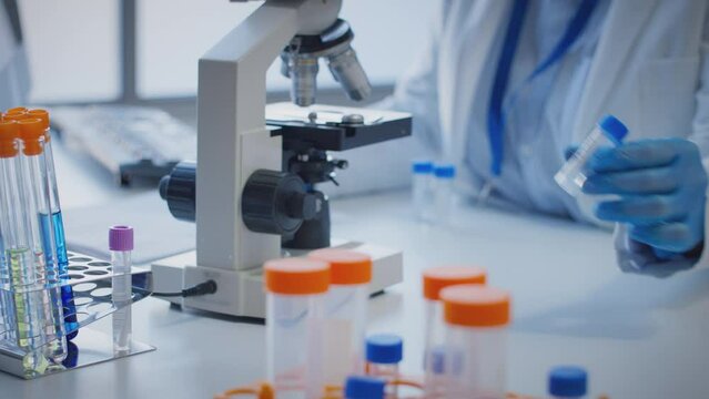 Close up of scientist wearing white coat looking through microscope and making notes whilst holding test tube which he puts on desk to show label delta - shot in slow motion