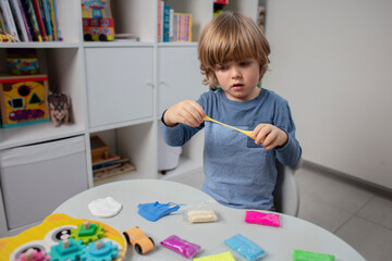 Beautiful toddler sculpt a plasticine and play with a wooden toys at home. Toddler play with a color educational toy and wooden car. Child play at the table in the baby room. Funny baby. 