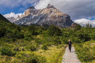 Woman hiking in Torres del Paine National Park with Los Cuernos and the Paine Massif behind,...