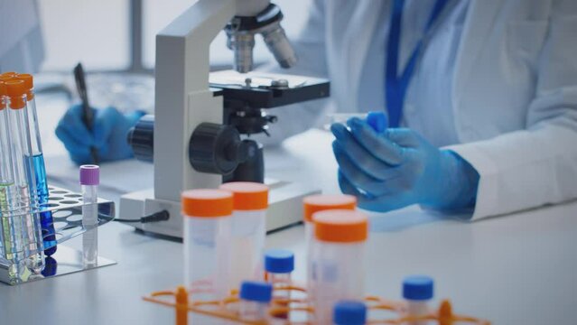 Close Up Of Lab Worker Conducting Research Using Microscope Holding Test Tube Labelled Zeta