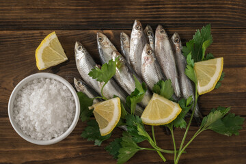 A bowl with coarse sea salt and sprat with herbs and lemon on a wooden table.