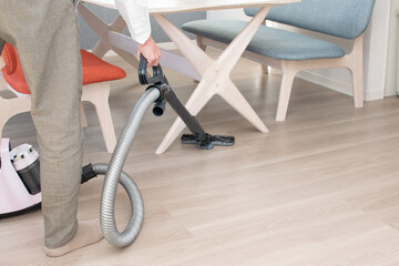 A Japenese young Asian man hoovers the floor using a vacuum cleaner in a house with a desk and two chairs