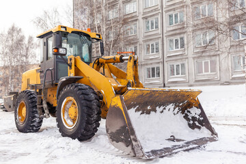 Big orange tractor cleans up snow from the road and loads it into the truck. Cleaning and cleaning of roads in the city from snow in winter. Snow removal after snowfall and blizzards. 