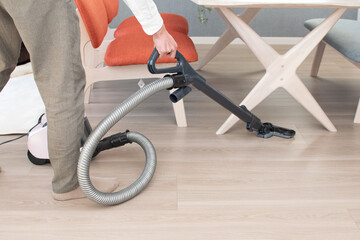A Japenese young Asian man hoovers the floor using a vacuum cleaner in a house with a desk and two chairs