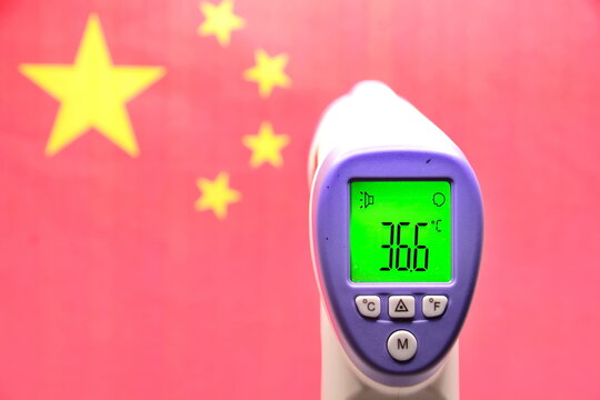 Concept of winter Games in 2022 in Beijing, China, due to threat of new coronavirus infection. Infrared thermometer shows normal healthy body temperature on blurred background of red Chinese flag