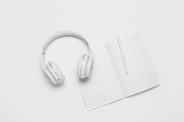 Modern headphones, notebook and pen on white background