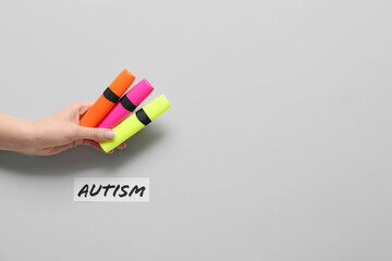 Female hand with colorful markers and word AUTISM on light background