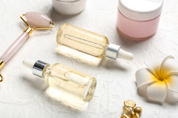 Fototapeta na wymiar Bottles of essential oil, facial massage tool and flower on light background, closeup
