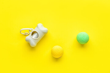 Dispenser with pet waste bags and balls on yellow background