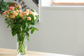 Vase with bouquet of beautiful fresh roses on table in room