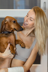 Portrait happy blonde girl with long hair holding cute purebred dog dachshund, close-up. High quality photo