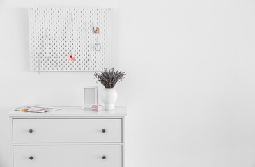 White chest of drawers with lavender bouquet and peg board on light wall background