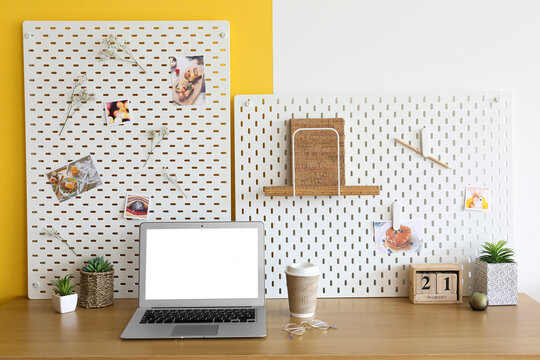 Stylish workplace with peg board on yellow and white wall background