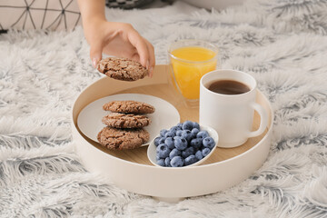 Woman taking cookie from tray with delicious breakfast on fluffy plaid