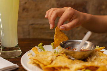 Close-up of a woman's hand grabbing a tortilla chip from a plate of nachos