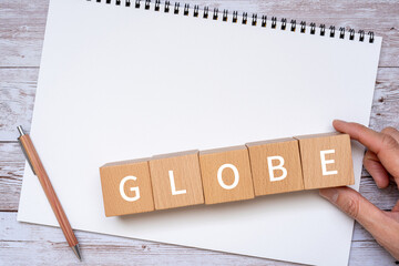 「GLOBE」と書かれた積み木とペン、ノート、人の手