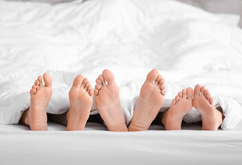 Feet of man and two women lying under blanket in bed. Polyamory concept