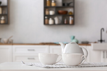 Fototapeta na wymiar Teapot with cups and napkin on table in light kitchen