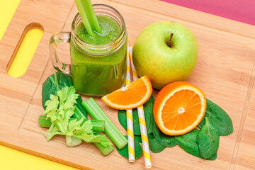 Fresh Green Smoothie of Apple, Celery, Spinach and Orange in Glass Smoothie Jar with Yellow Cocktail Straw on Wooden Cutting Board. Vegan Detox Drink. Vegetarian Culture. Healthy Eating and Fruit Diet