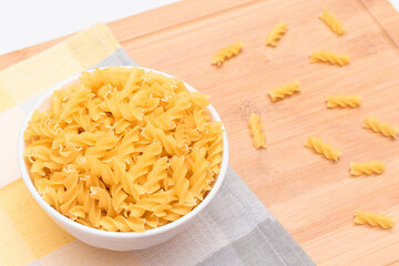 Uncooked Fusilli Pasta in White Bowl on Wooden Board. Raw and Dry Macaroni. Unhealthy and Fat Food. Italian Culture