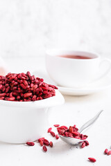 Bowl and spoon with dried barberries on light background