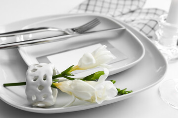 Beautiful table setting for wedding, blank card and flowers on light background, closeup