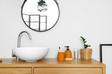 Fototapeta na wymiar Wooden table with sink and bath supplies near light wall in room
