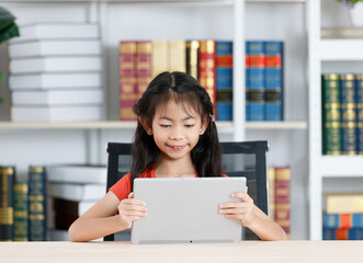 Fototapeta premium Asian clever smart diligent young primary school girl daughter in casual outfit wearing big headphone smiling using touchscreen tablet computer in hands learning studying online during quarantine