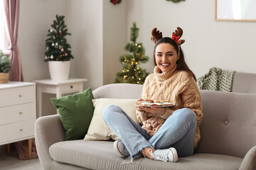 Happy young woman holding plate with tasty gingerbread cookies at home