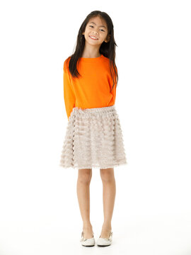 Full body cutout isolated studio shot of Asian young primary schoolgirl model in casual orange shirt and skirt outfit standing on white background