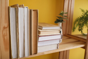 Wooden shelf with books near yellow wall, closeup