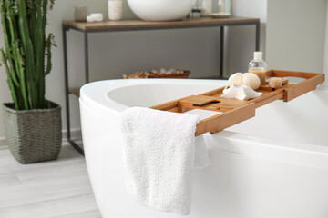 Wooden tray with accessories and candle on bathtub in room