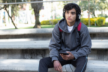 Fototapeta premium lonely and sad young man listening to music in the park with his headphones, his face is melancholic and depressed.