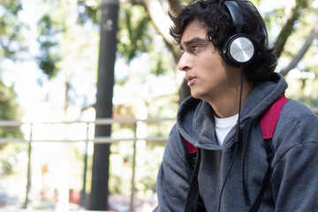 young man enjoying some time alone relaxing listening to music with his headphones in the park, he has a smile on his face and a facial expression of peace and well-being.